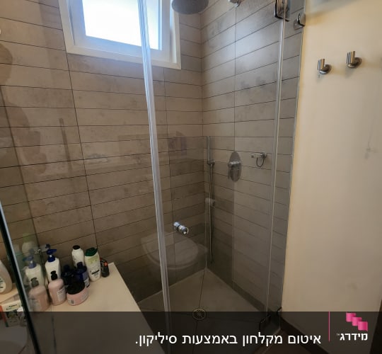 מקלחת עם ראש מקלחת, דלת זכוכית ומוצרי טיפוח